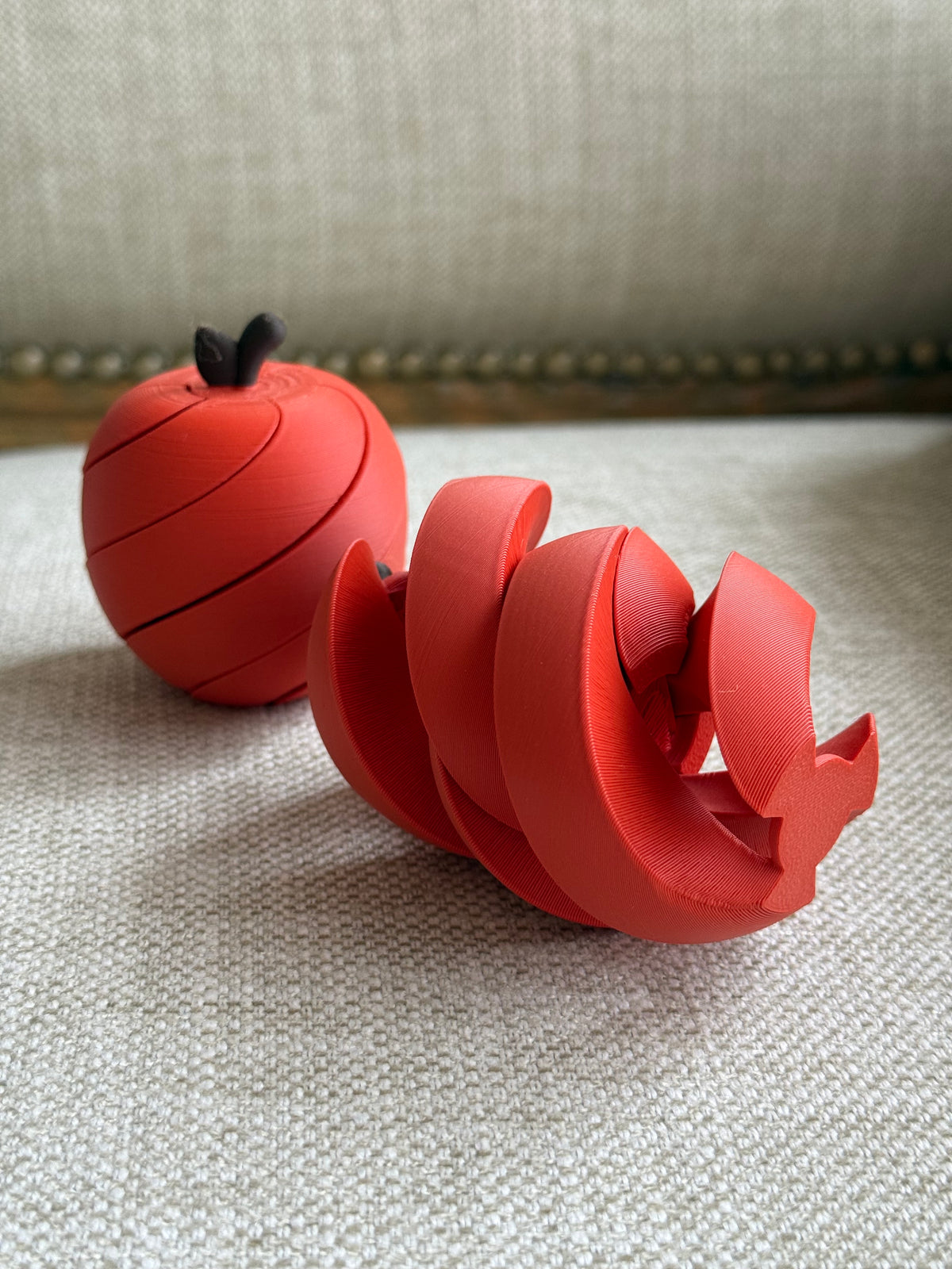 Expanded spiral apple fidget toy beside a rounded apple on textured fabric